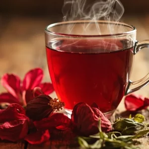 فنجان چای ترش در کنار گل‌های خشک هیبیسکوس و برگ چای